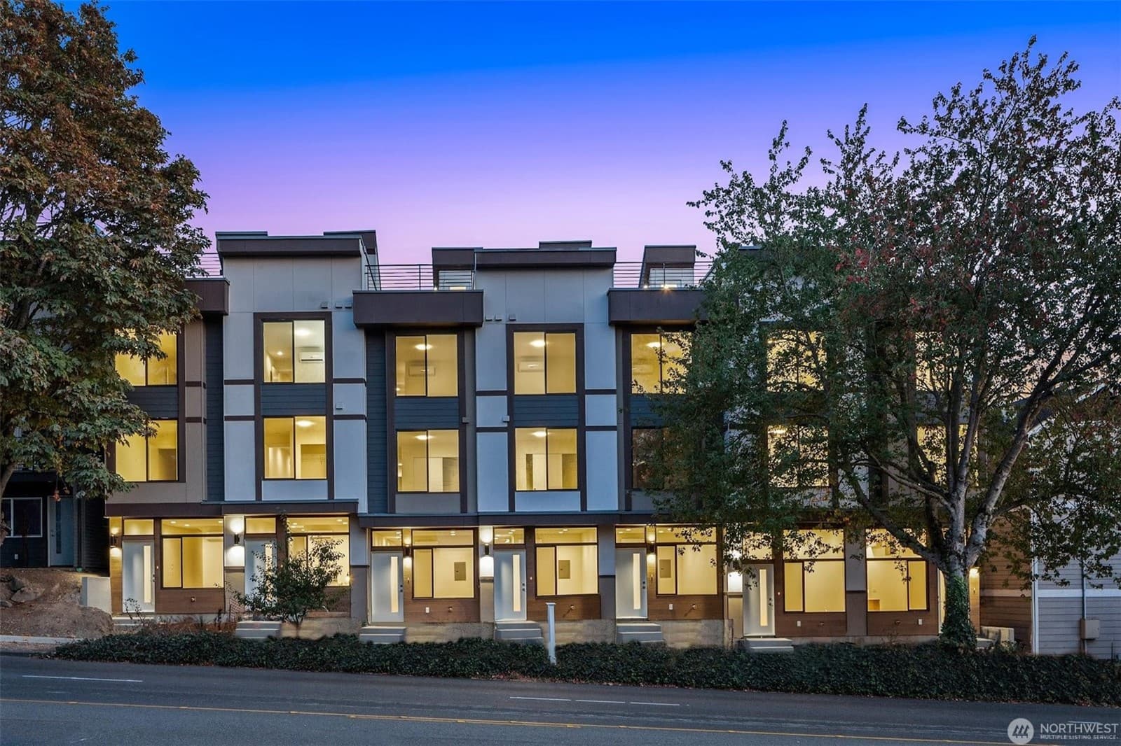 The townhouse row at dusk, windows lit across three storeys