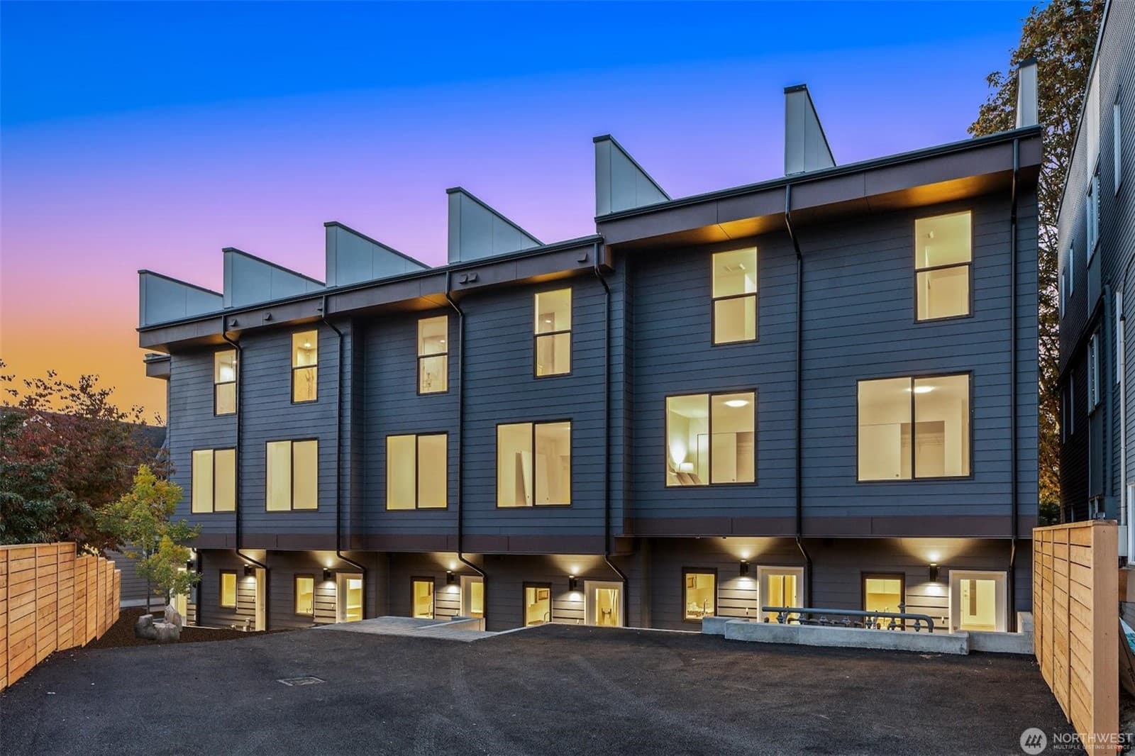 Rear elevation at dusk, its sawtooth roofline above dark siding