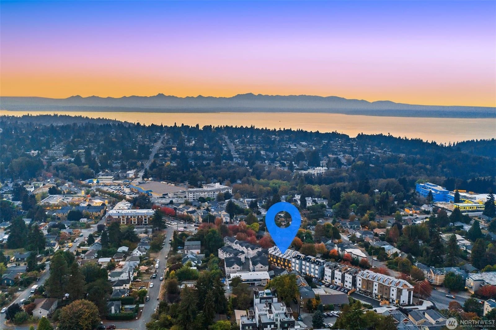 Aerial over the neighborhood at sunset, water and mountains on the horizon, the property marked