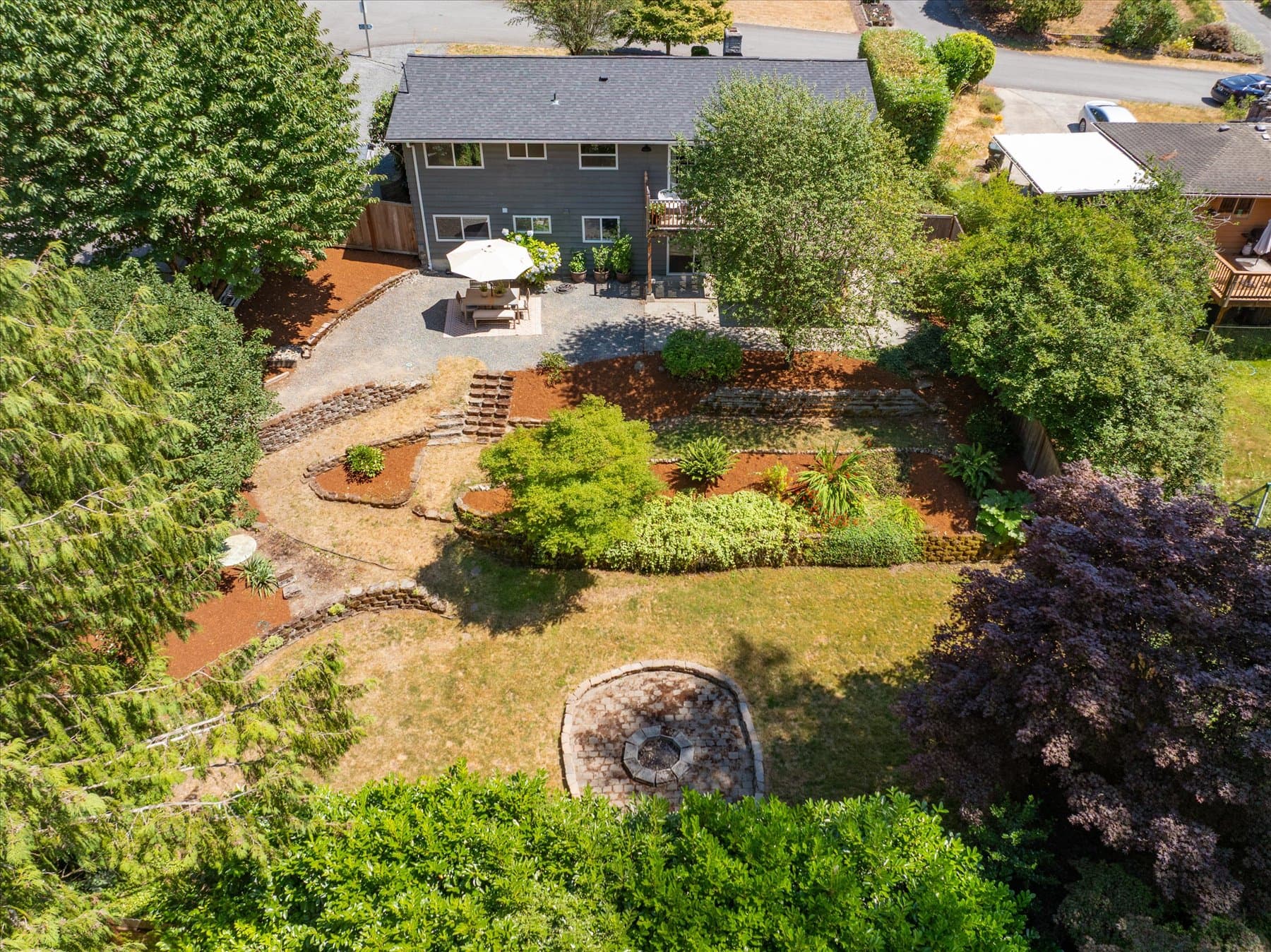 Aerial view of the terraced back yard, with stone retaining walls, lawn and a circular firepit below the house