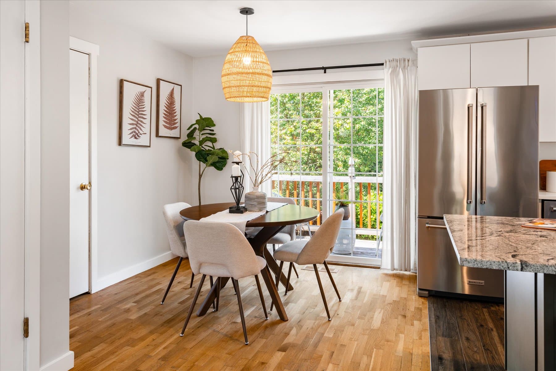 Dining area under a woven pendant, with the slider to the deck and stainless refrigerator beyond