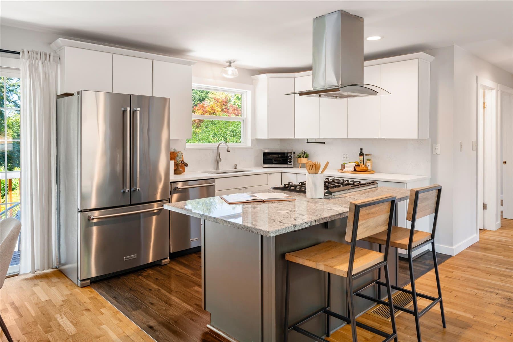Remodeled kitchen with a granite island and bar seating, stainless appliances, gas cooktop and wall-mounted hood
