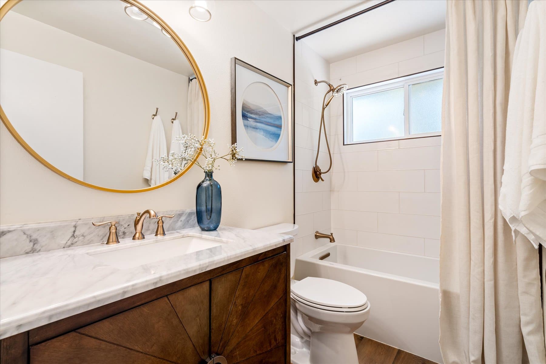 Updated bathroom with a marble-topped vanity, round mirror and tub-shower