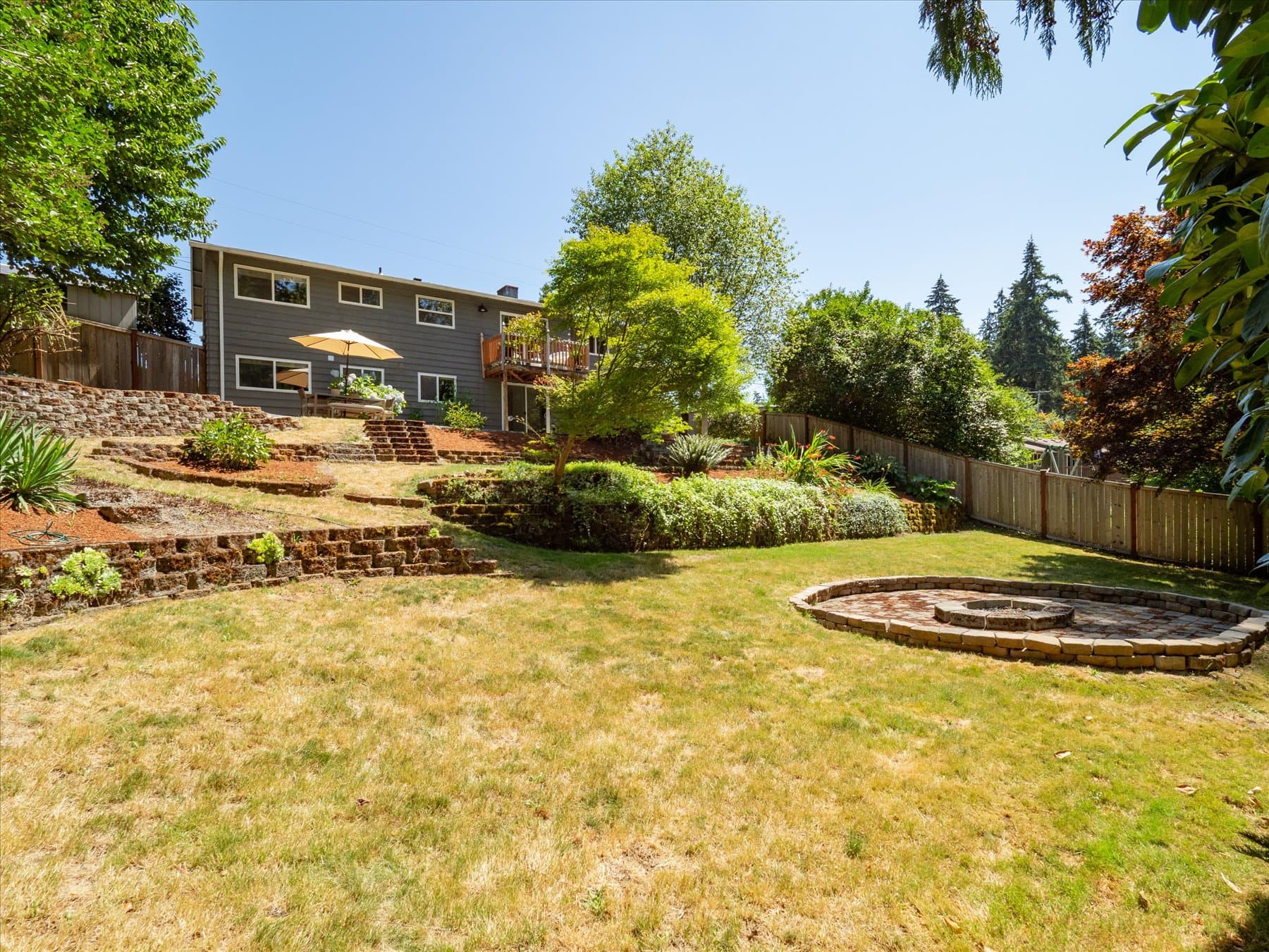 Terraced back yard with lawn, stone walls and firepit, looking back up toward the house