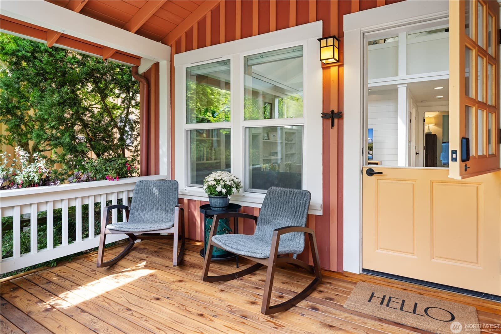 Covered cedar front porch with two rocking chairs, a white railing, a craftsman lantern and a yellow Dutch door standing open