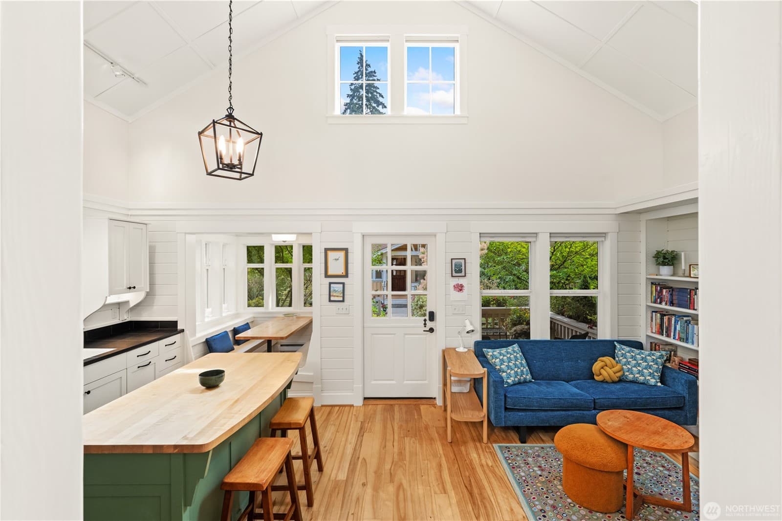 Vaulted great room with clerestory windows, a maple-topped green island with stools, and a blue sofa beside built-in bookshelves