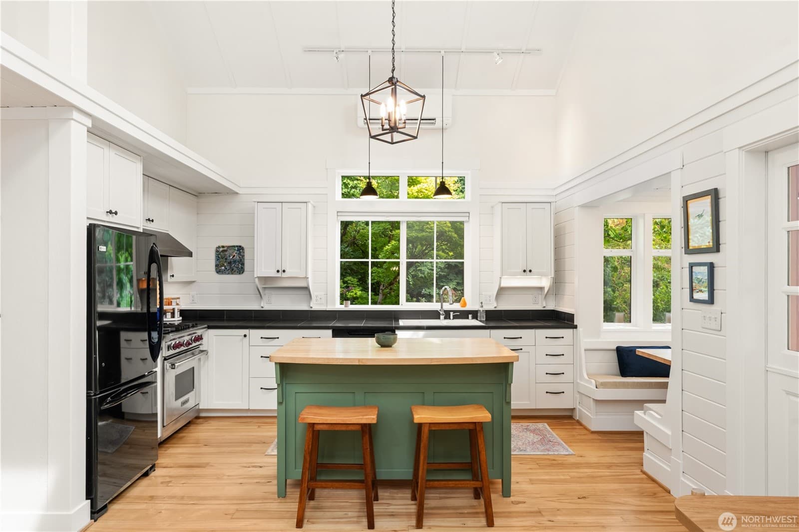 White shiplap kitchen with a green island, maple butcher-block top, Wolf range, black counters and a window onto the trees