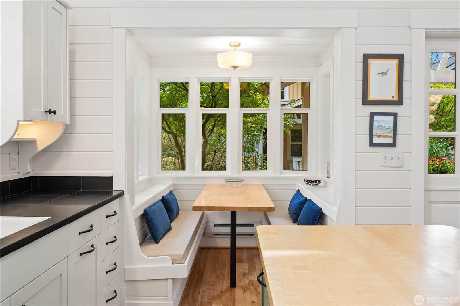 Built-in breakfast nook with a maple table and cushioned benches under a bank of windows looking into the garden