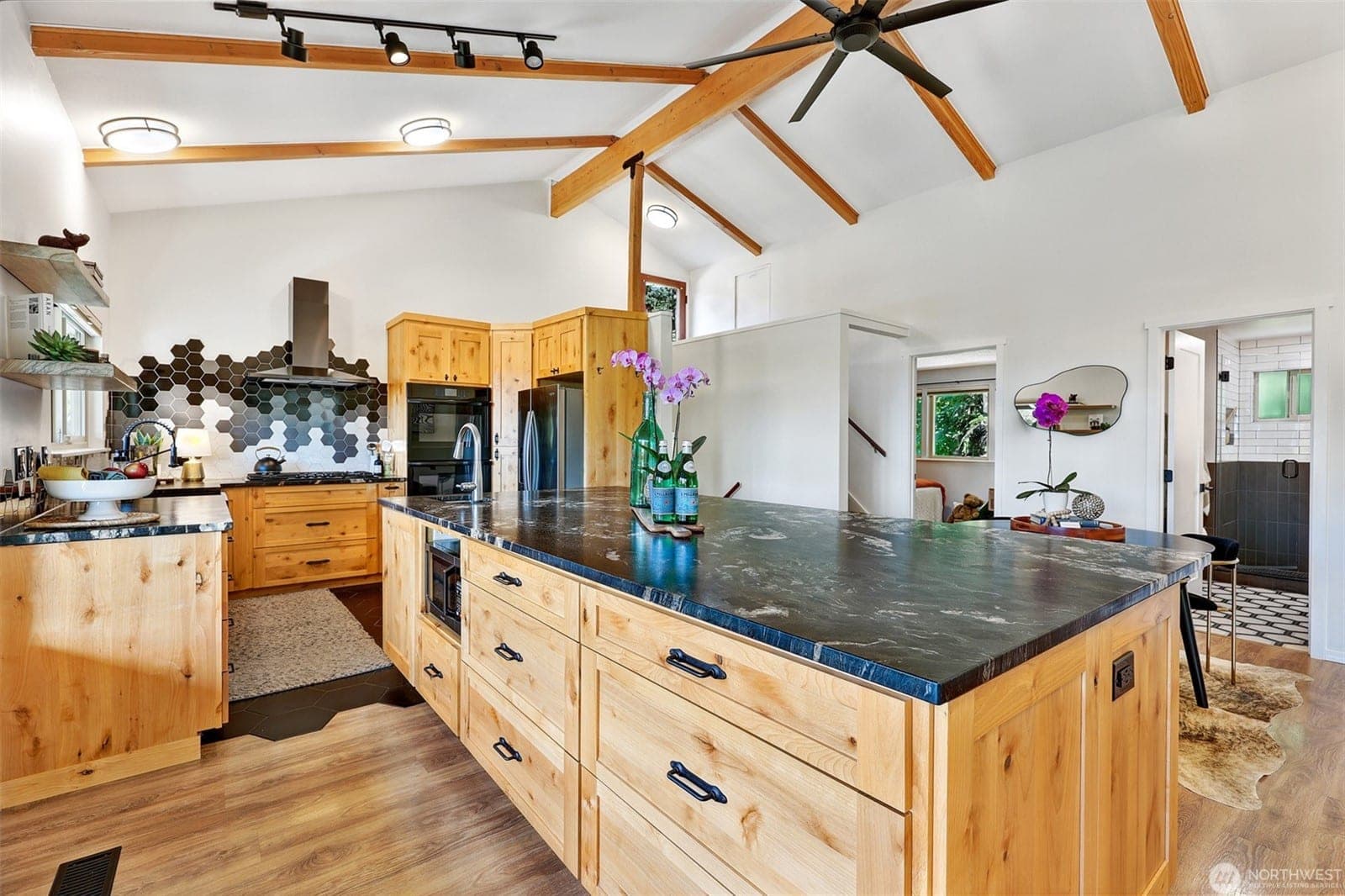 Remodeled kitchen under a vaulted, beamed ceiling, with a long alder island topped in dark granite and a hexagon tile backsplash