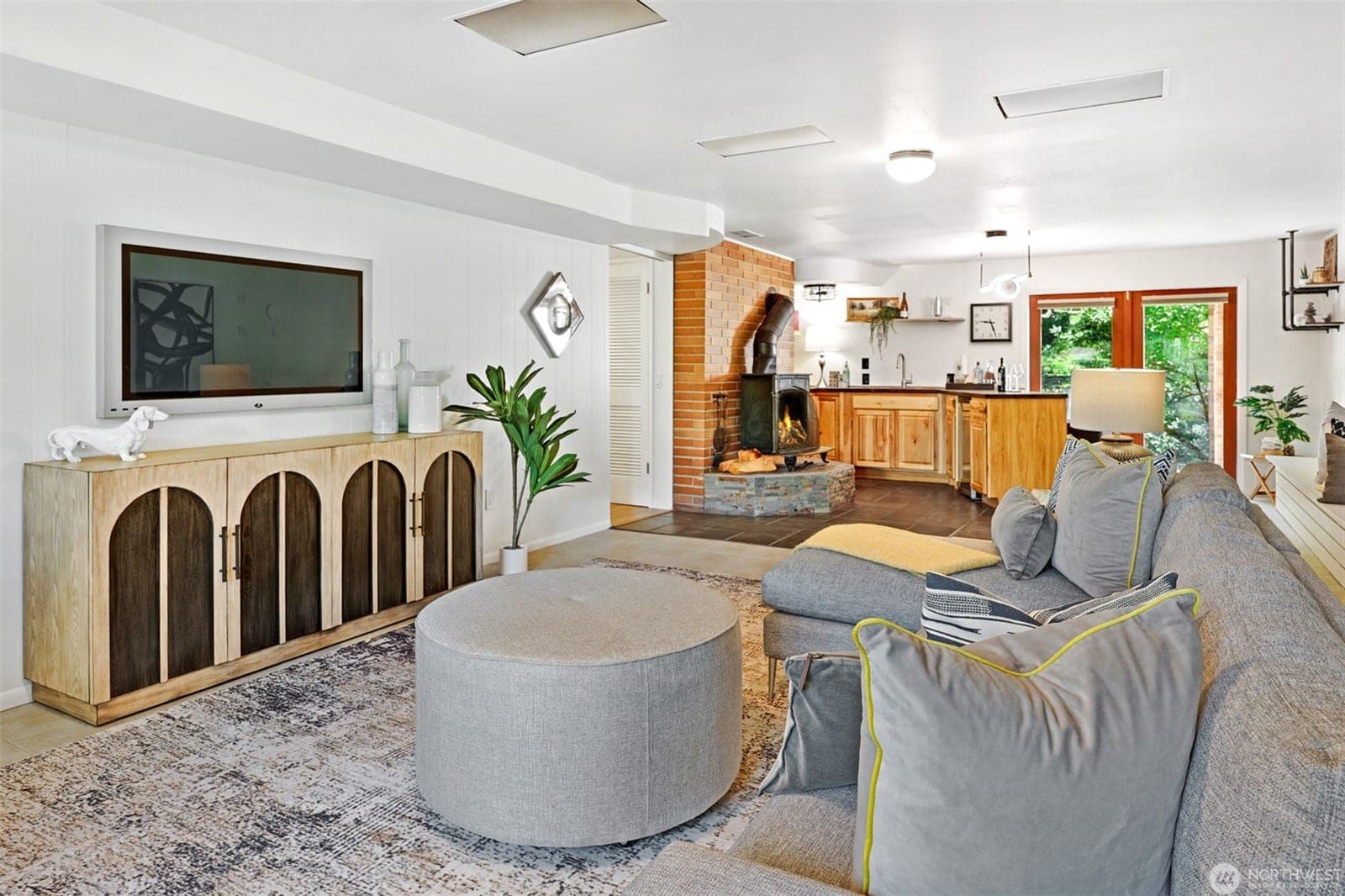 Lower-level family room with a sectional, looking toward a brick wall with a wood stove and the second kitchen