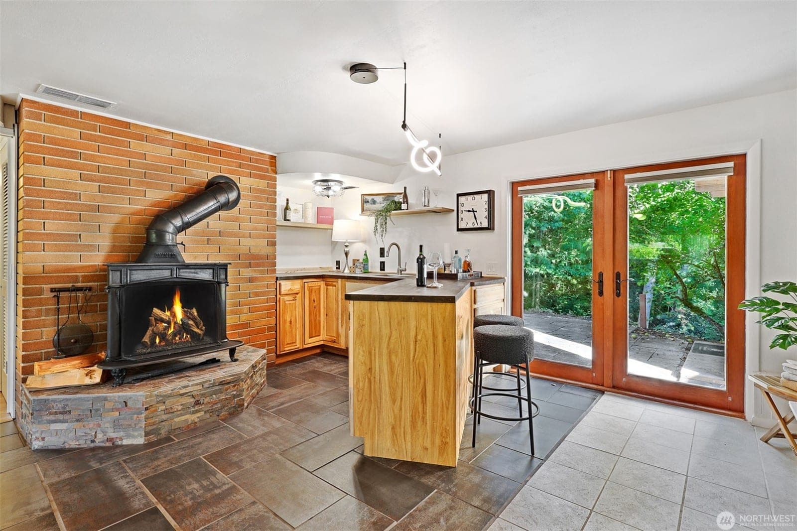 Wood stove on a stone hearth against a brick wall, beside the lower-level bar and French doors to the patio