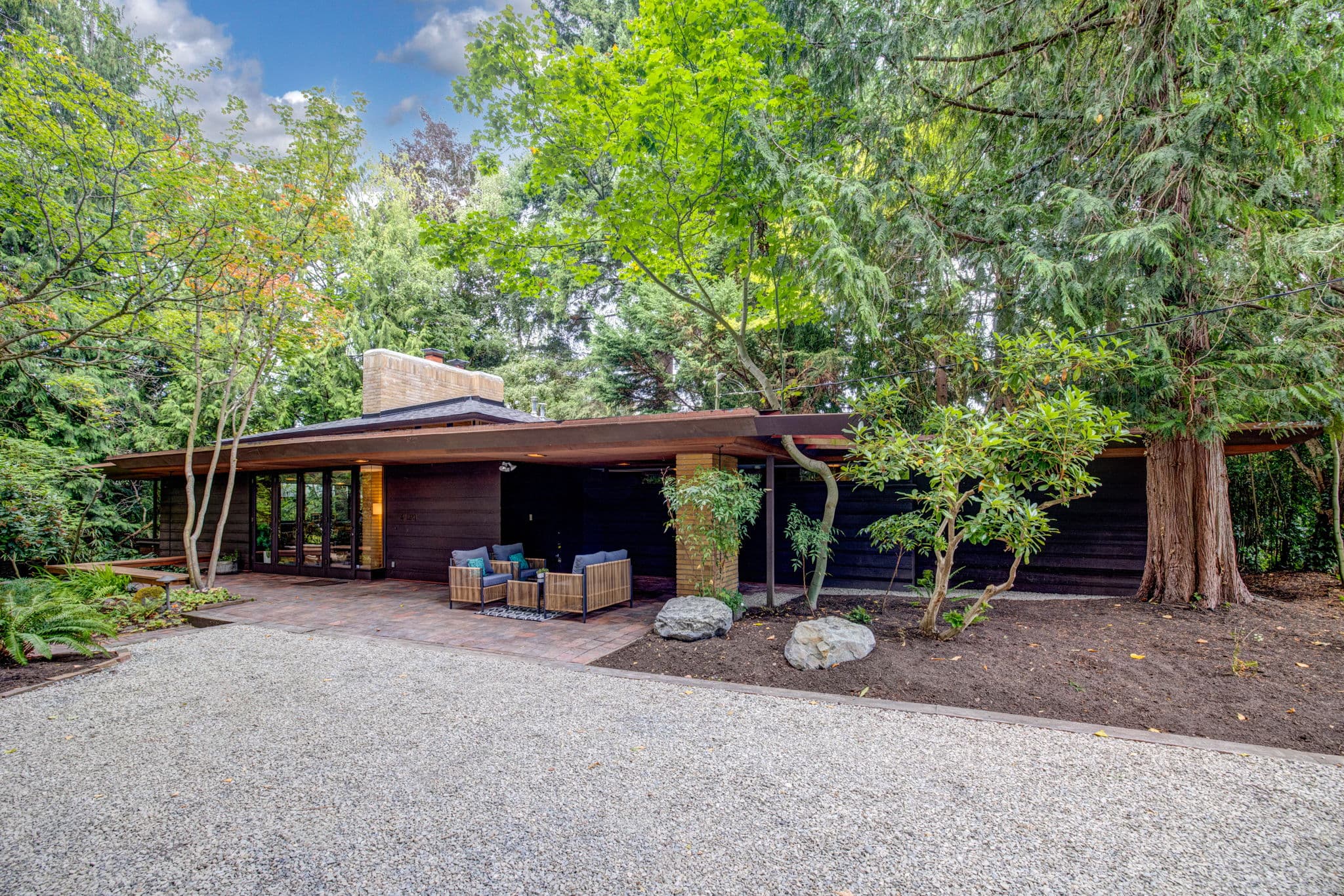 The house from the drive, its low horizontal roofline set among firs