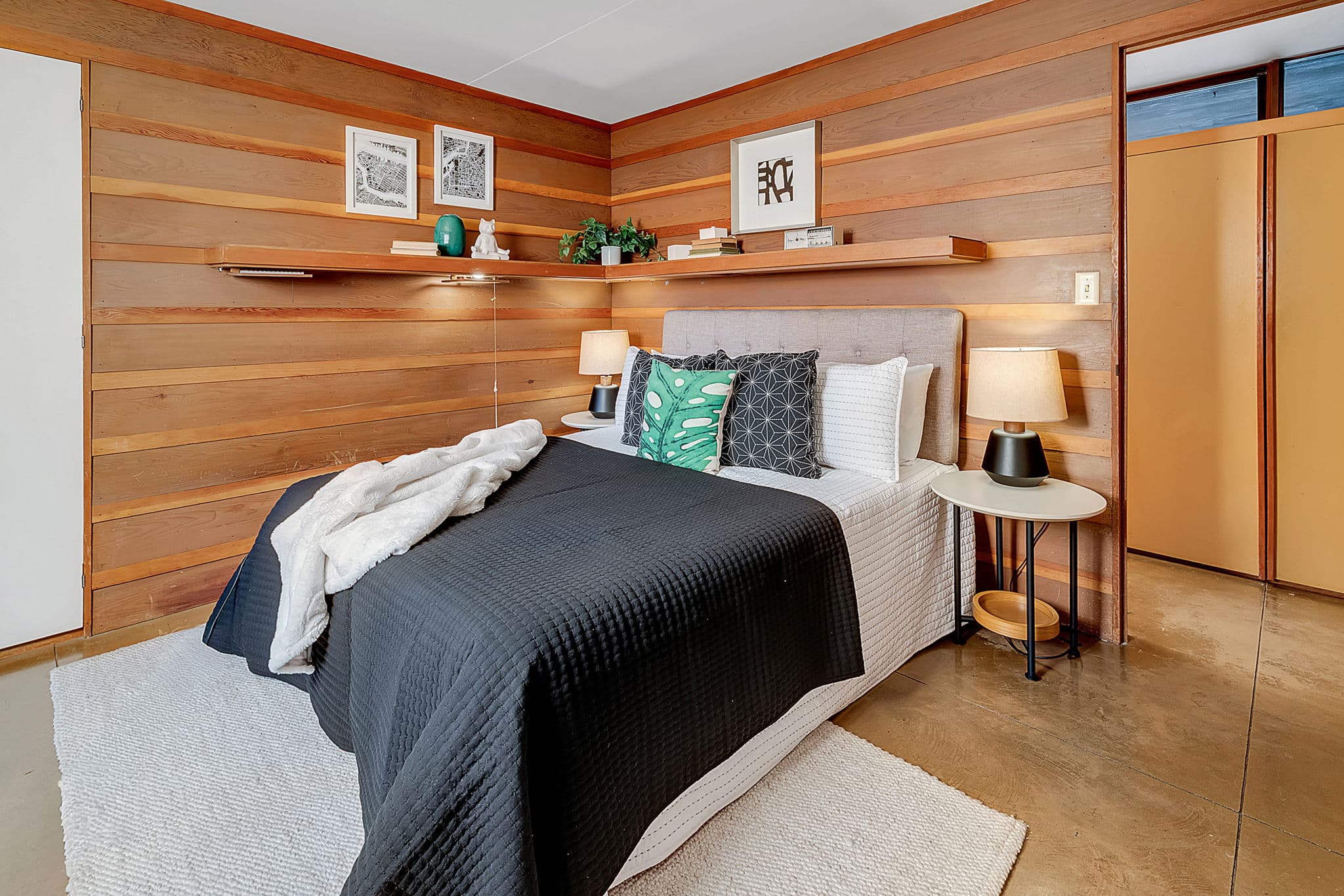 Bedroom panelled in wood, with a floating shelf above the bed