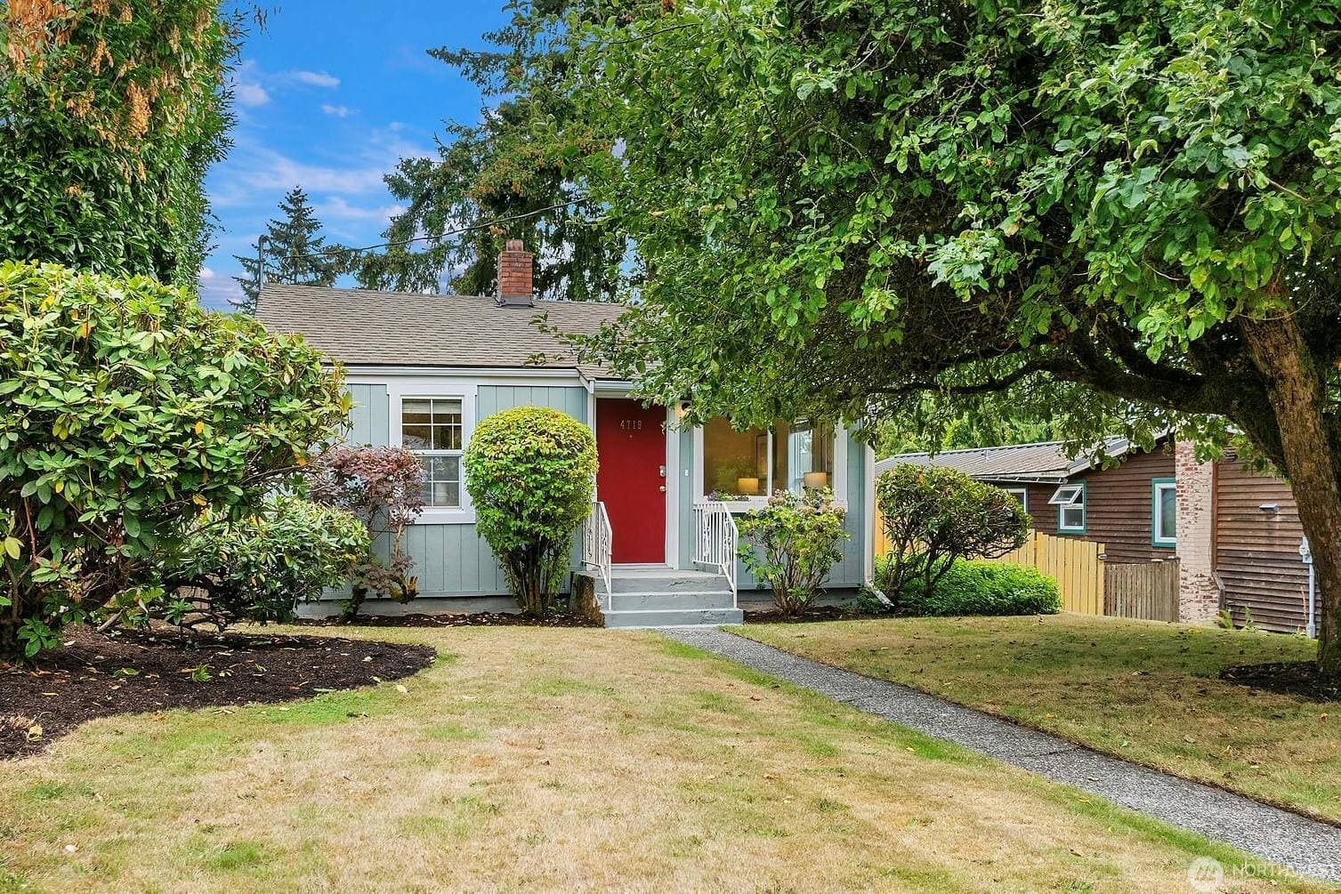 The pale-blue cottage from the front walk, with its red door, white railings and rhododendrons under a big shade tree