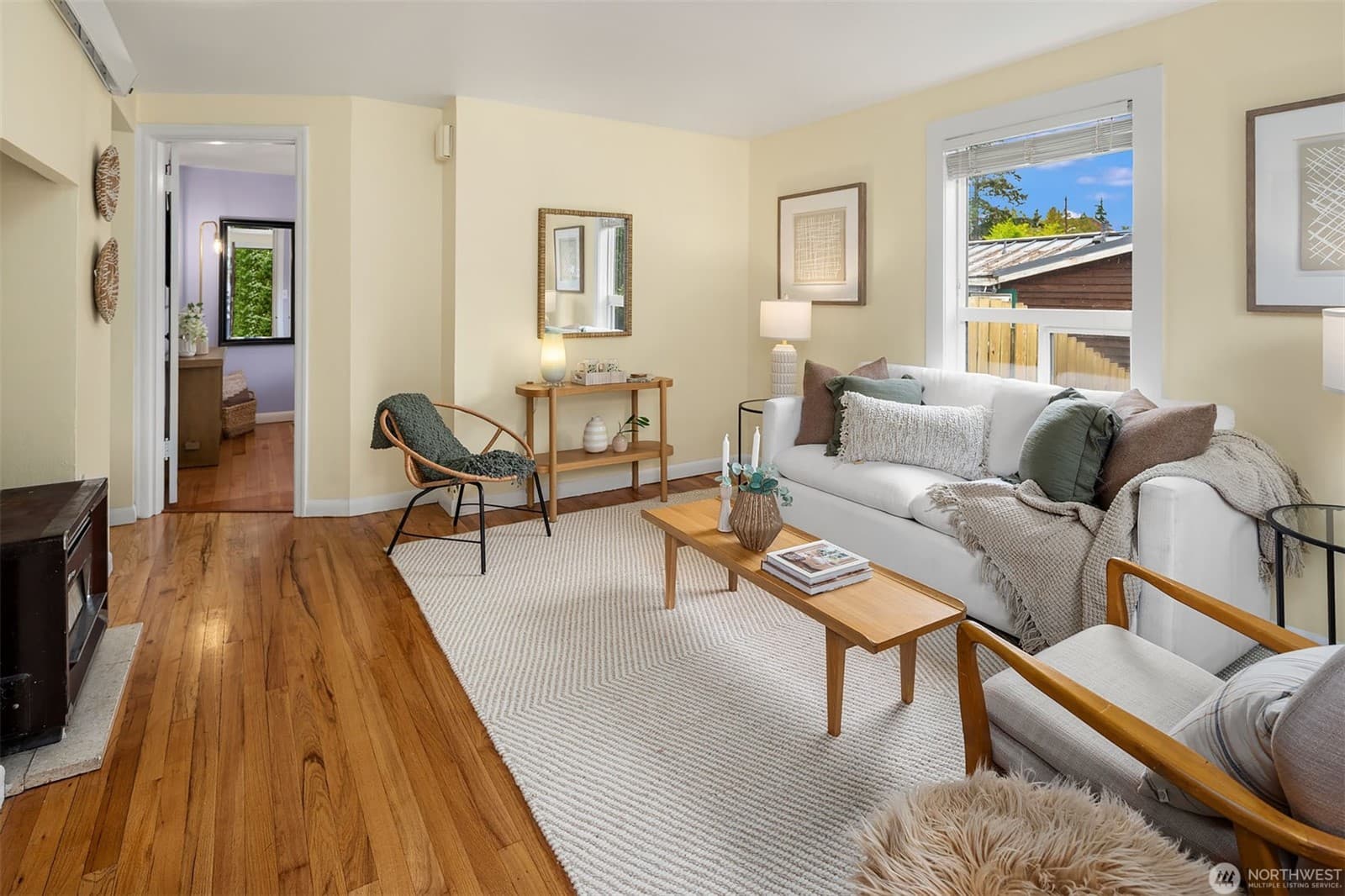 Living room with original oak floors, a wood stove and a window onto the side yard, a bedroom visible through the doorway