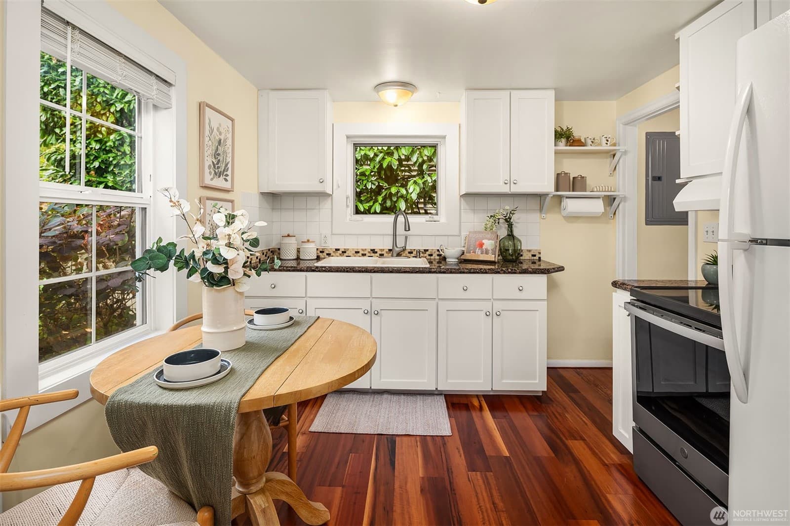 Kitchen with white shaker cabinets, a granite counter and a window over the sink, beside a small dining table