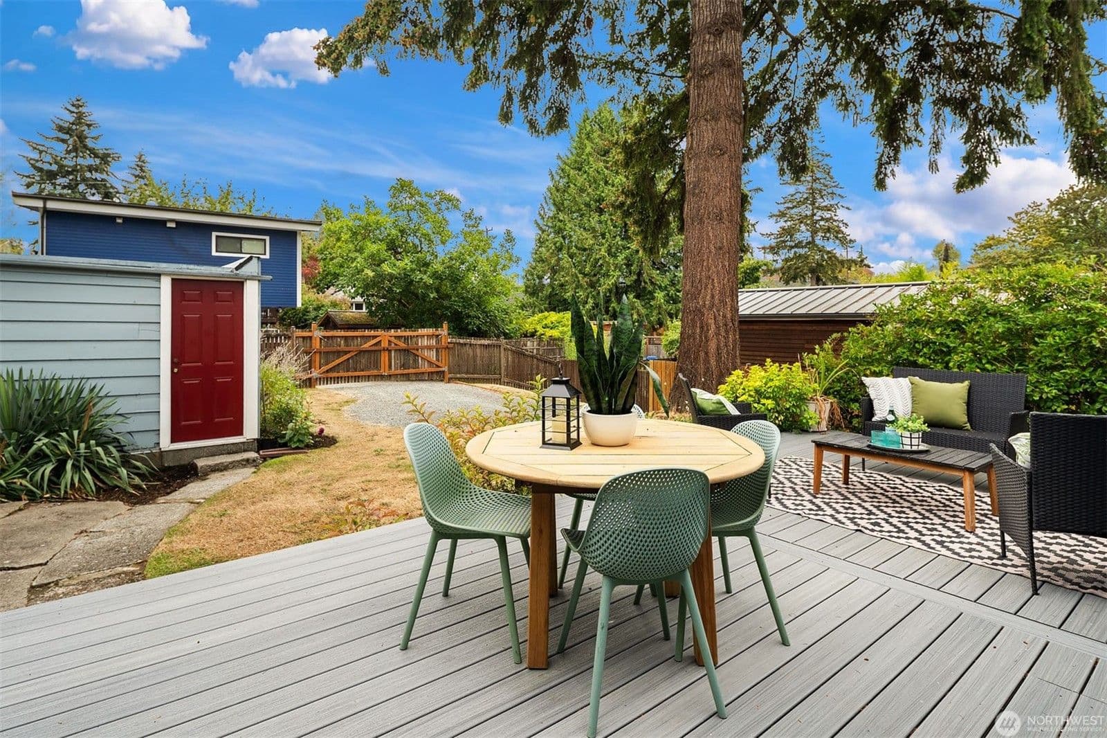 The new deck set for dinner under a tall fir, with the lawn, gravel parking pad and garage door beyond