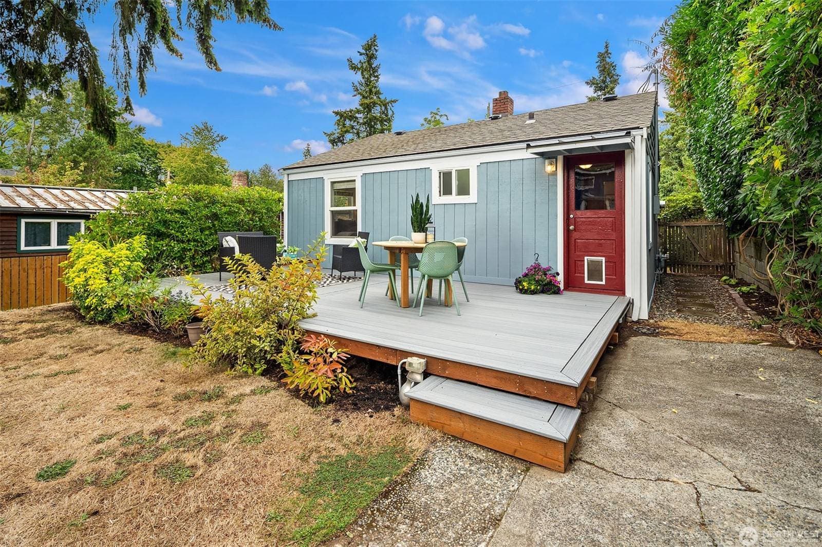 Back of the cottage with the red back door opening onto the new deck and the paved parking area