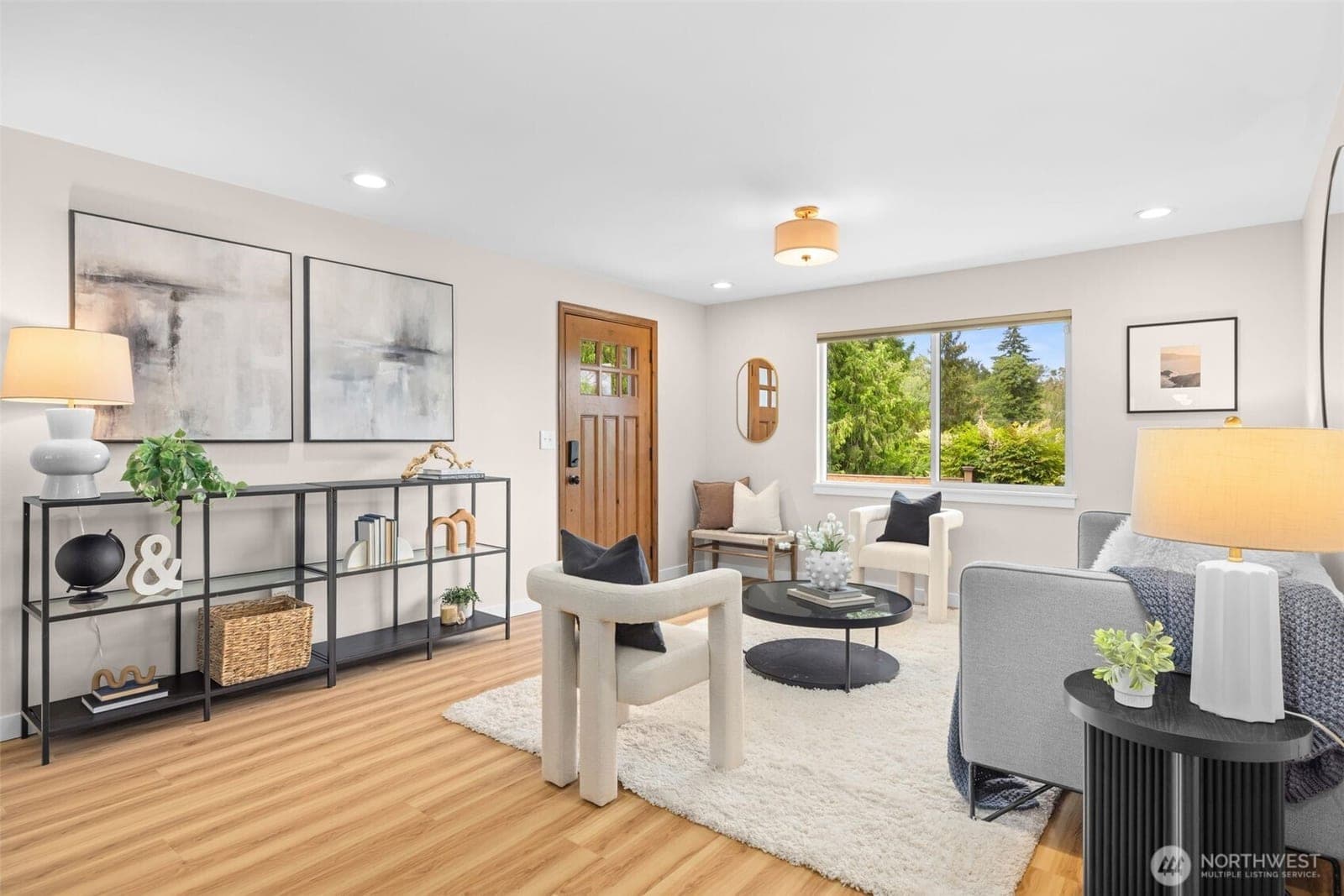 Living room with the wood front door, black shelving along one wall and a wide window onto the greenery