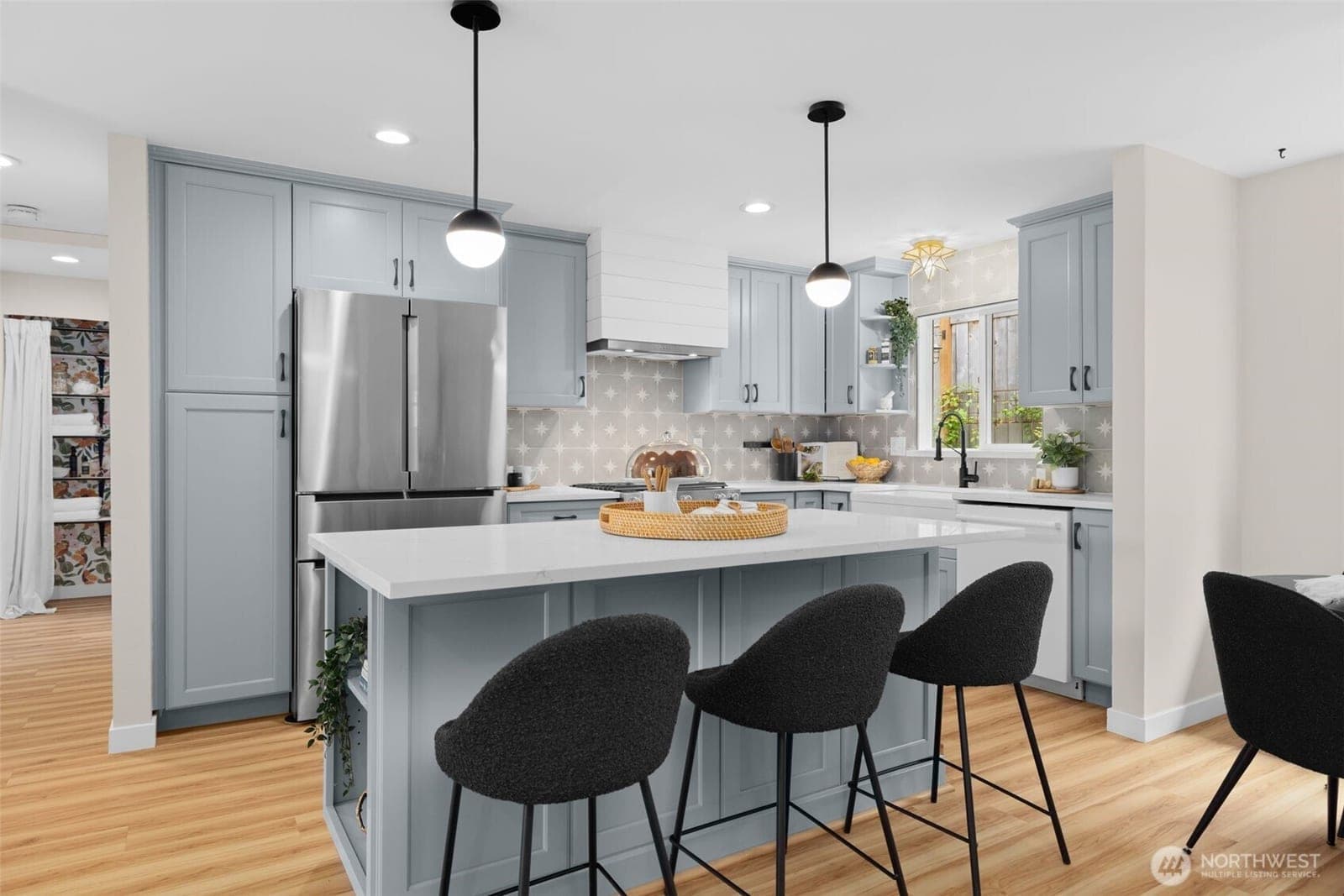 Remodeled kitchen with pale-blue cabinets, a quartz island with bar stools, patterned tile backsplash and stainless refrigerator
