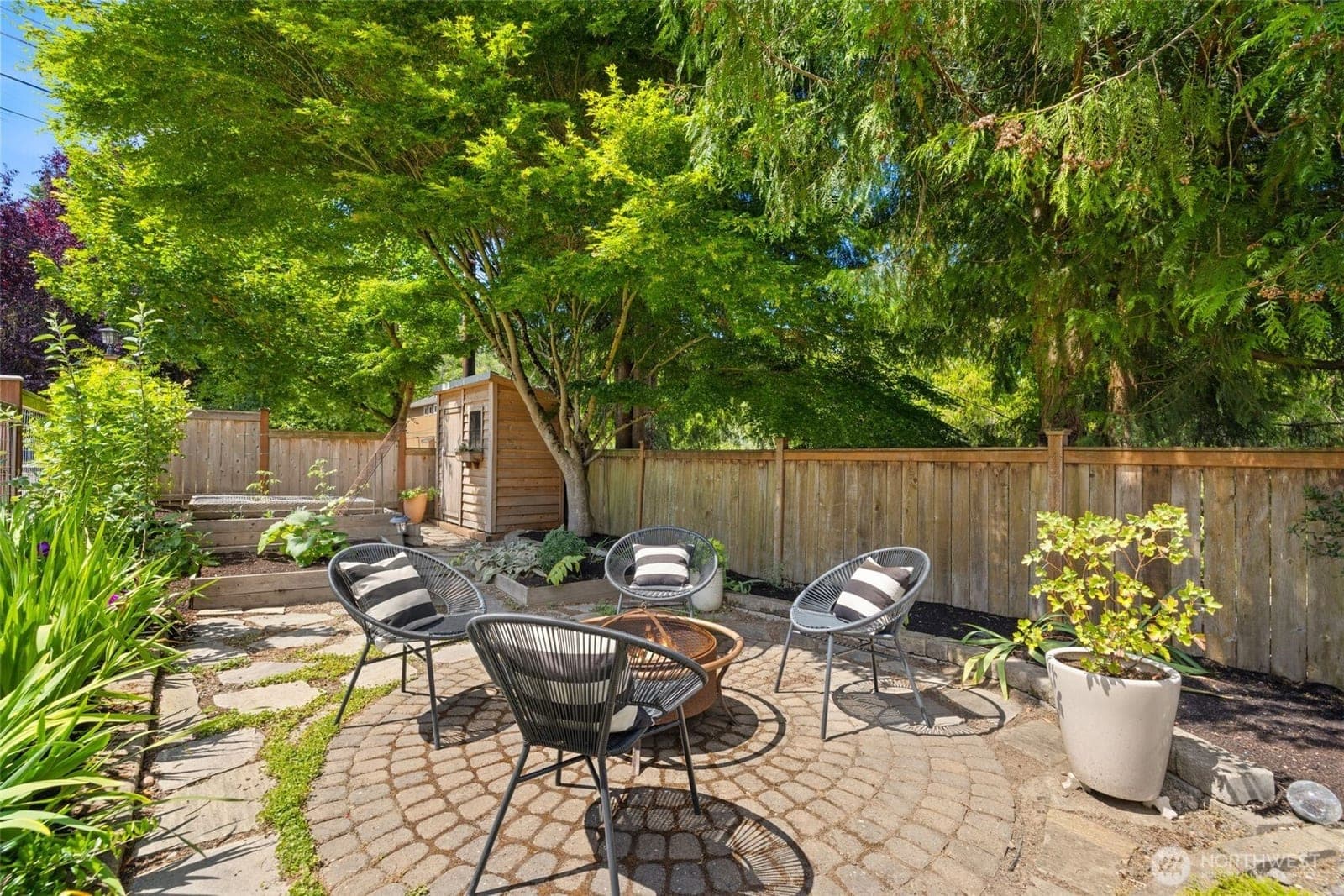 Fenced back yard with a paver patio, firepit seating and a garden shed under mature trees