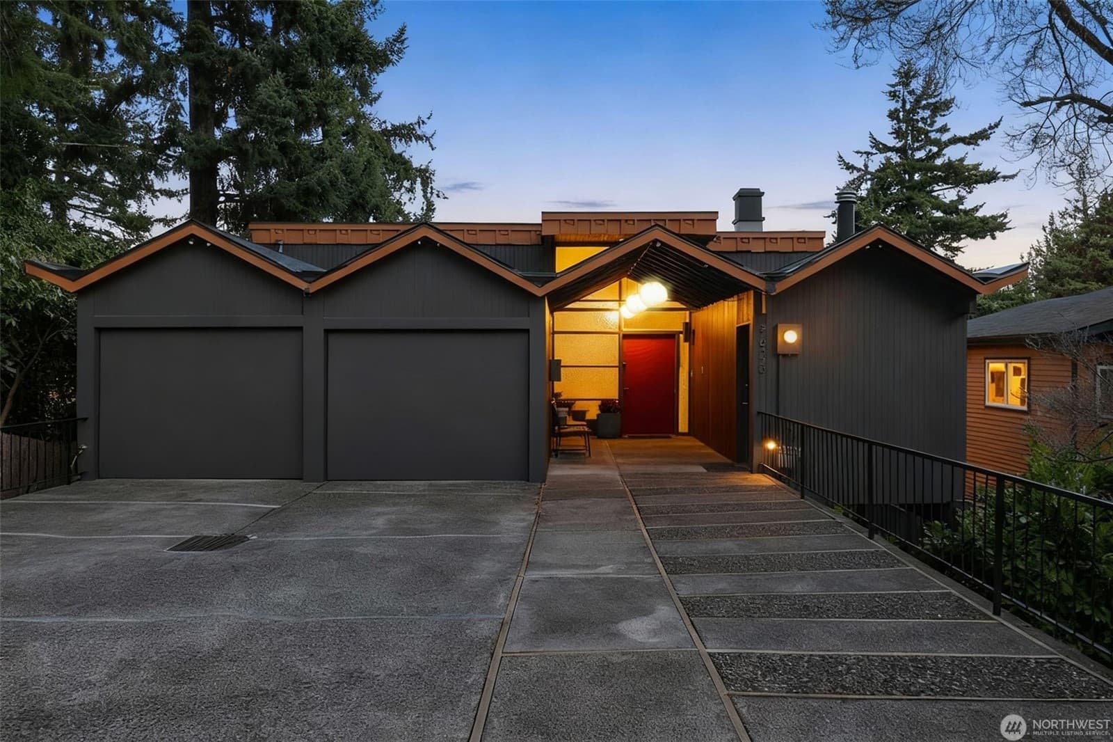 Approach from the street at dusk, with the dark-clad garage and a lit entry beyond
