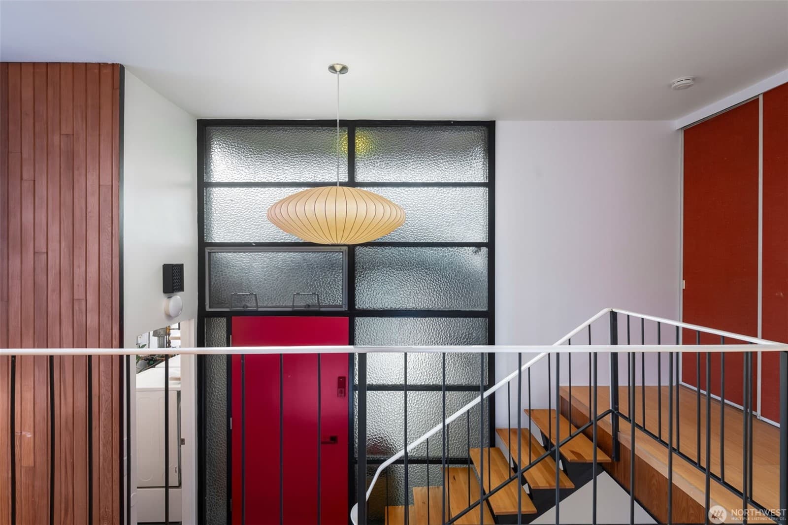 Stair landing with a red door and gridded glass panels under a saucer pendant