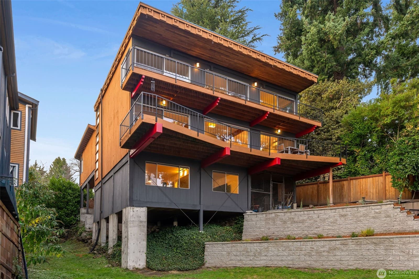 The house from the garden at dusk, its cantilevered decks and red accents stacked over three levels
