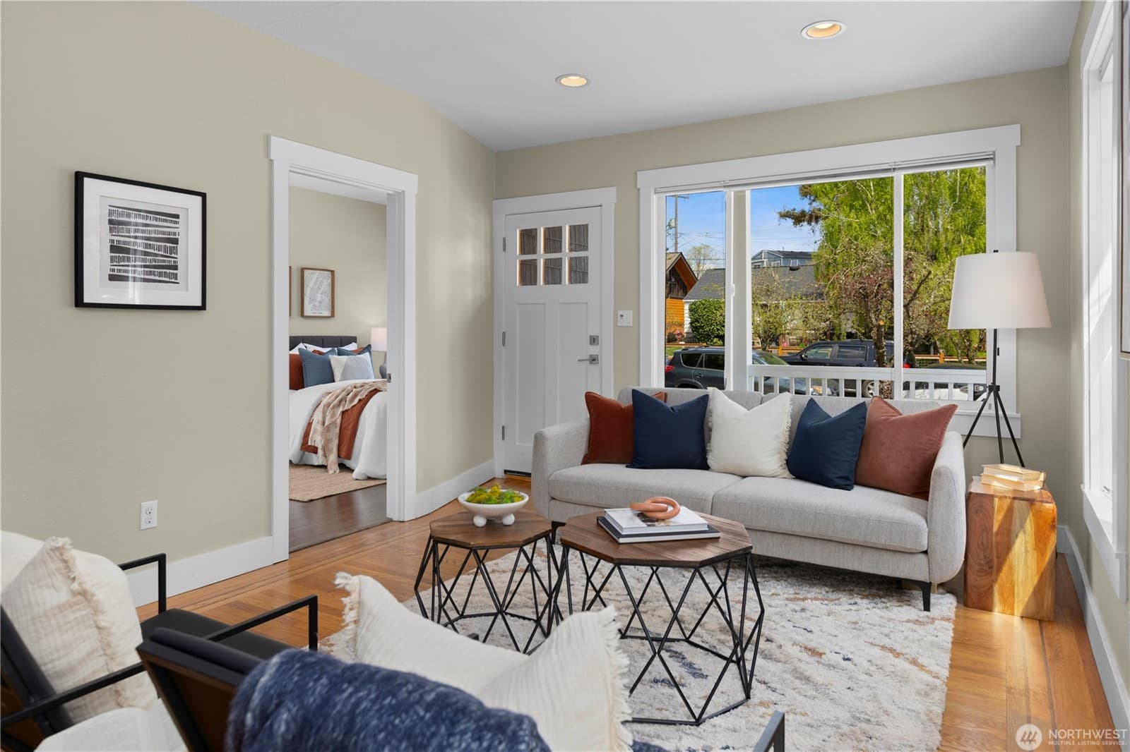 Living room with a wide front window, looking through to a bedroom beyond