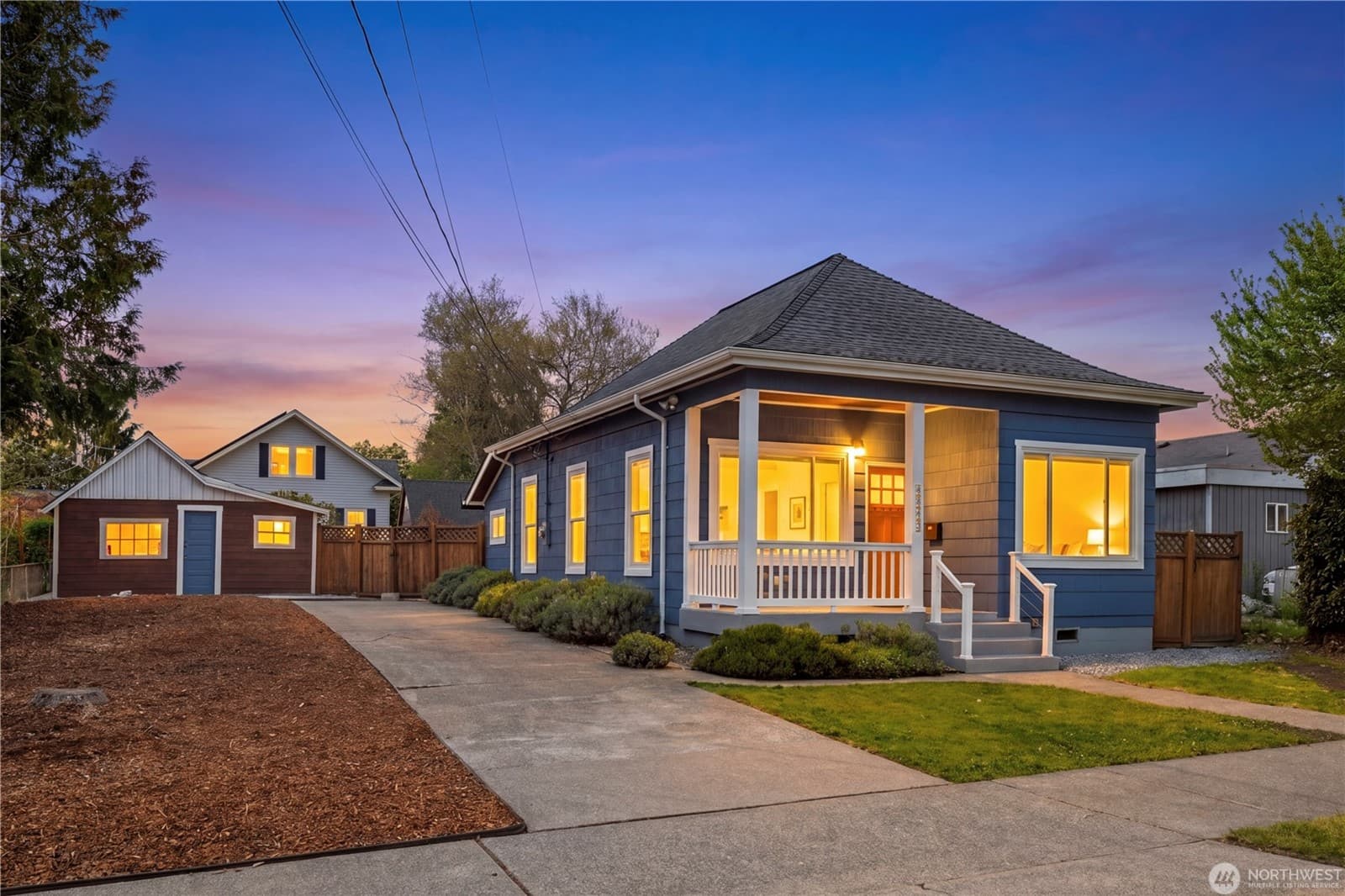 The blue 1905 cottage at dusk, its porch and windows lit from within