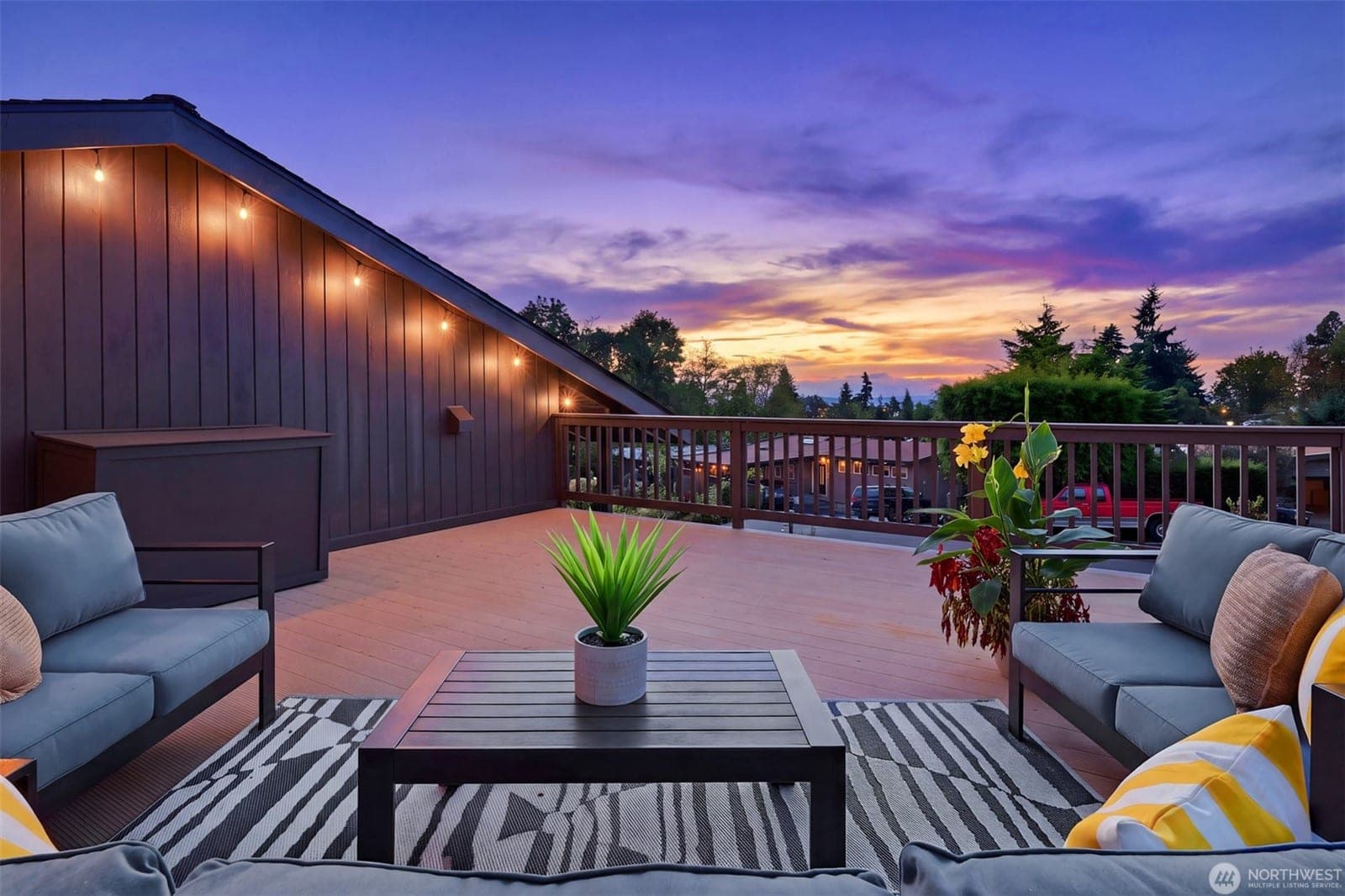 The deck at dusk, with outdoor sofas under string lights and a violet sunset over the trees toward the Sound